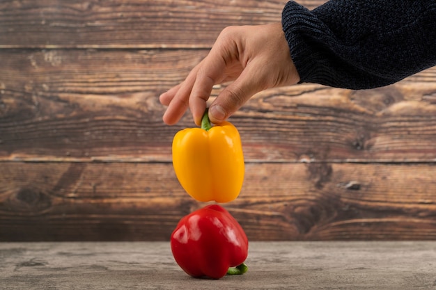 Female hand holding ripe bell peppers on wooden surface