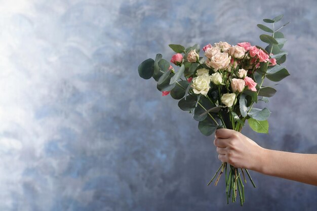 Female hand holding roses bouquet on grey background