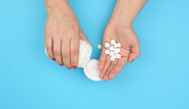 Female hand holding round white pills on a blue background