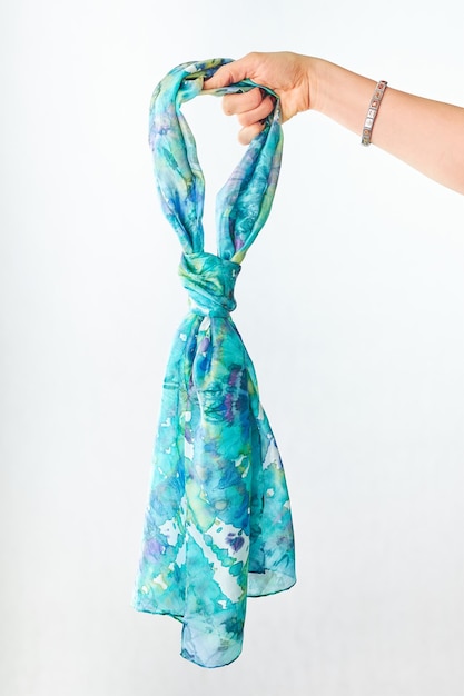 Female hand holding silk colourful hand painted tied scarf over grey background