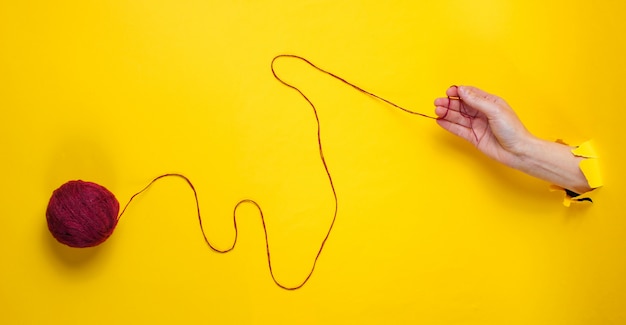Female hand holding skein of thread through torn yellow paper. Minimalistic creative medicine concept