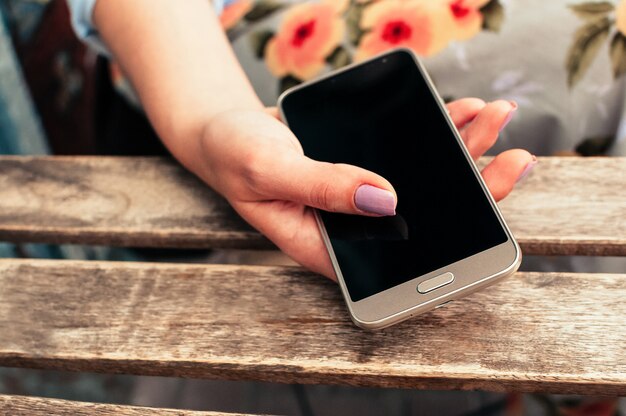 Female hand holding smart phone with blank screen, at table