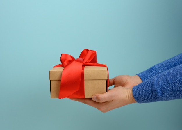 Female hand holding a square box tied with a red ribbon, surprise