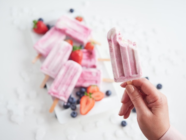 Female hand holding a strawberry ice cream popsicle with a bite missing