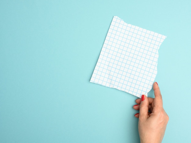 Photo female hand holding a torn blank sheet of paper in a cage on a blue background