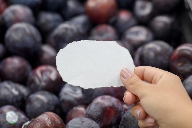 Female hand holding torn piece of paper in front of shelf with Spanish plums