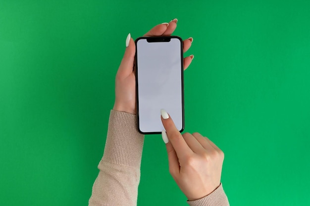 Female hand holding and touching on mobile smartphone with white screen Isolated on green Photo template for any images on mobile phone display Layout with easily removable phone monitor background