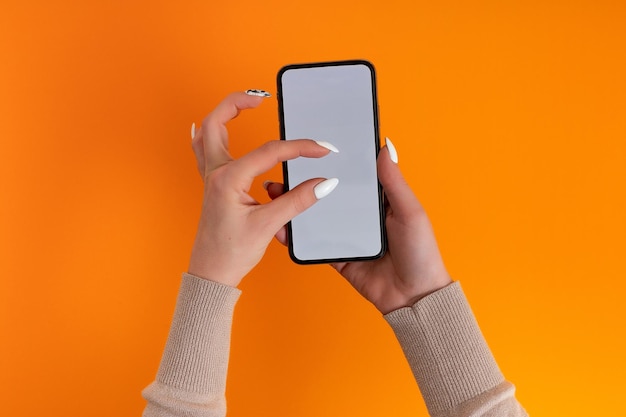 Photo female hand holding and touching on mobile smartphone with white screen isolated on orange photo template for any images on mobile phone display layout with easily removable phone monitor background