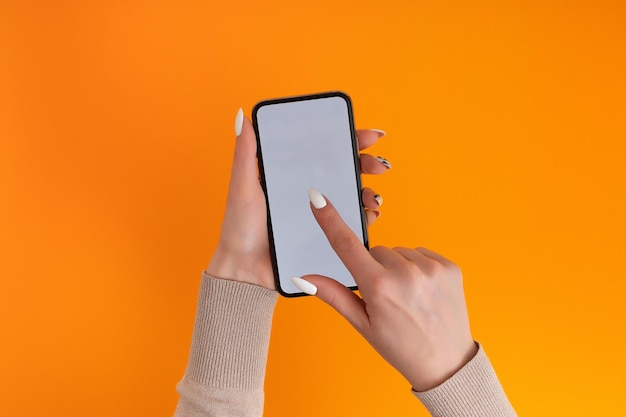 Female hand holding and touching on mobile smartphone with white screen Isolated on Orange Photo template for any images on mobile phone display Layout with easily removable phone monitor background