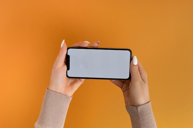 Female hand holding and touching on mobile smartphone with white screen Isolated on Orange Photo template for any images on mobile phone display Layout with easily removable phone monitor background