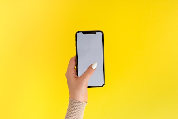 Женская рука держит и прикасается к мобильному смартфону с белым экраном, изолированным на желтом. Шаблон фотографии для любых изображений на дисплее мобильного телефона. Макет с легко съемным фоном монитора телефона.