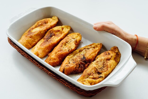 Female hand holding a tray with torrijas a typical spanish sweet fried toasts of sliced bread soaked in eggs and milk on white background