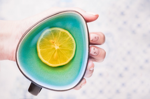 Female hand holding a turquoise cup of lemon tea