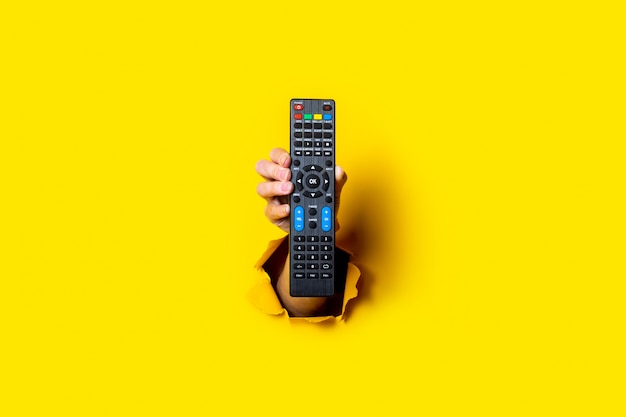 Female hand holding a TV remote control on a bright yellow background