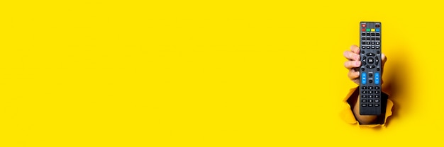 Foto mano femminile che tiene un telecomando della tv su uno sfondo giallo brillante
