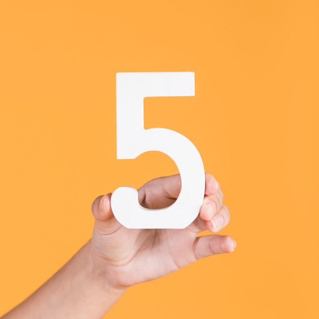 Photo female hand holding up the number 5 against a yellow background