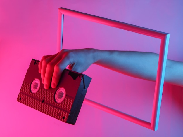 Женская рука держит видеокассету через парящий кадр с неоновым голографическим светом