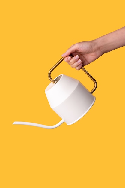 Female hand holding watering can pot like pouring on bright yellow background