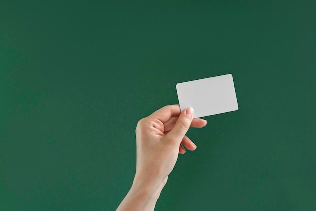 Photo female hand holding white credit card isolated on green background. close up christmas gifts buying