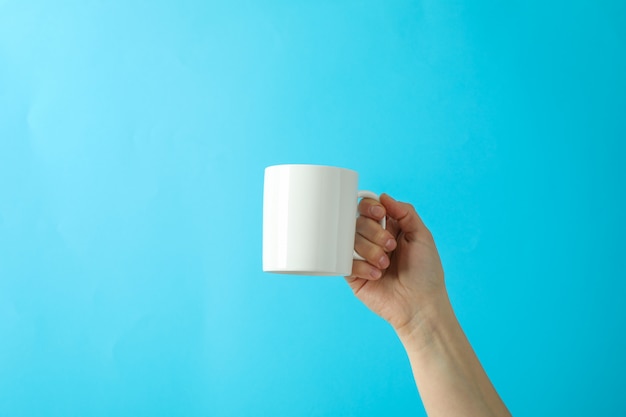 Female hand holding white cup against color background