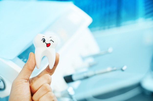 female hand holding a white toy tooth on the surface of dental equipment at dentistry clinic. oral care concept