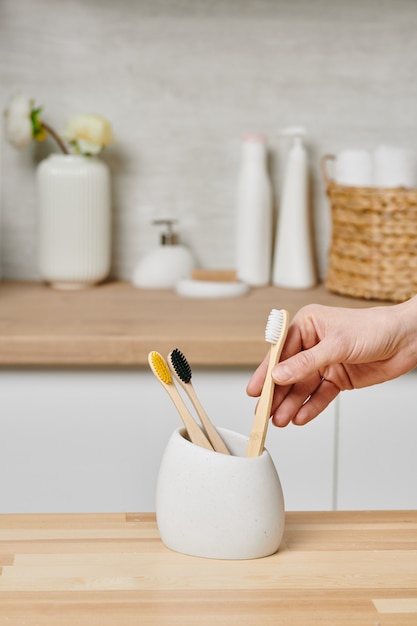 Female hand holding wooden toothbrush in a white cup in bathroom