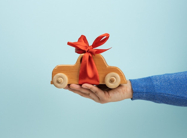 Female hand holding wooden toy car with red ribbon, auto insurance concept, loan