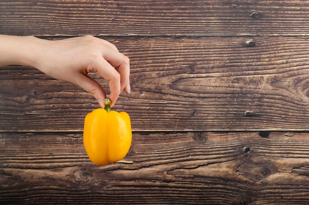 Female hand holding yellow bell pepper on wooden surface