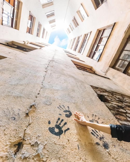 Female hand holding on yellow wall. Near black handprints of human hands. Photo from bottom to top. On background enclosed courtyard-well, windows and blue cloudy sky. Yard in Saint Petersburg.