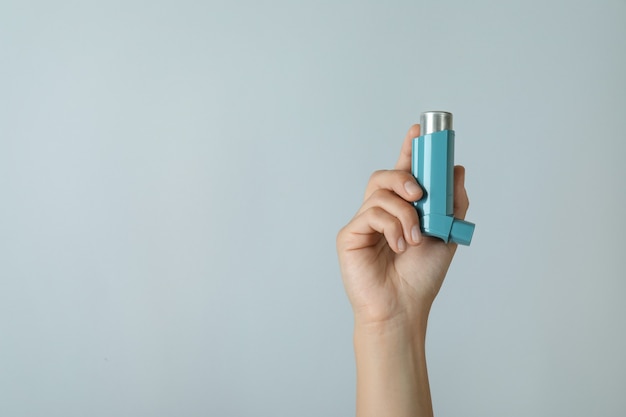 Female hand holds asthma inhaler on light gray background