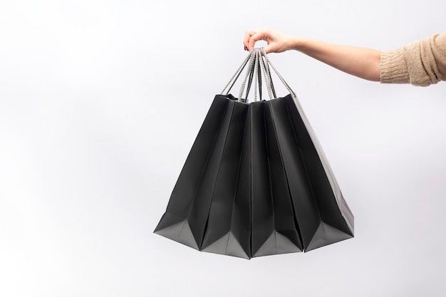 Female hand holds black paper shopping bags isolated on white background.