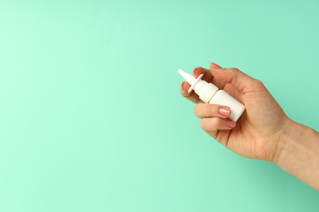 Female hand holds blank bottle of nasal spray on mint background