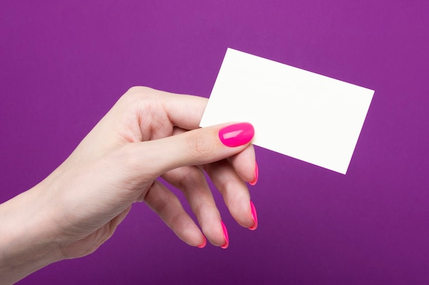 Female hand holds a blank business card on a purple background.