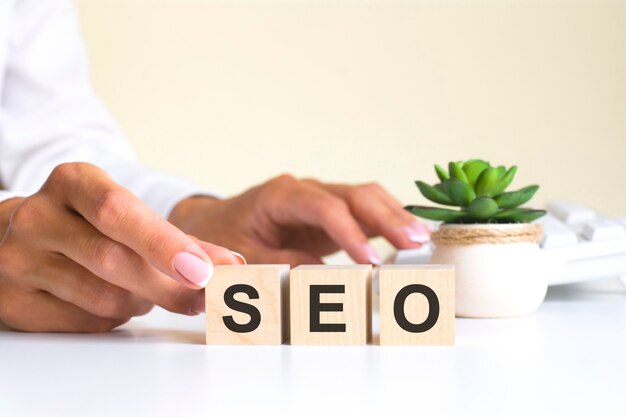 Female hand holds a block with the letter S from the word SEO. the word is located on a white office table on the background of a white keyboard. financial, marketing and business concepts