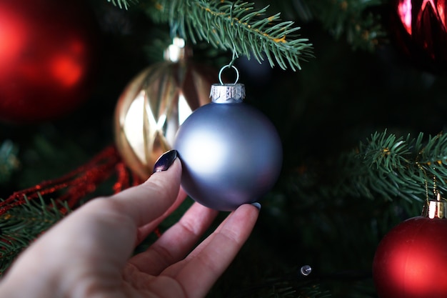 女性の手は、クリスマスツリーの背景に青いクリスマスボールを保持します。