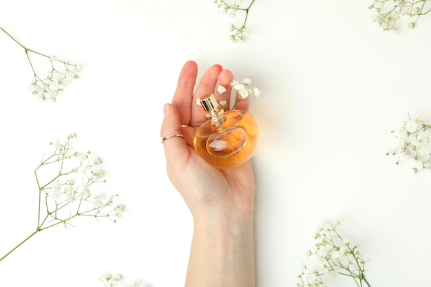 Female hand holds bottle of perfume on white background with flowers