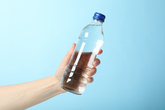 Female hand holds bottle with water on blue, close up