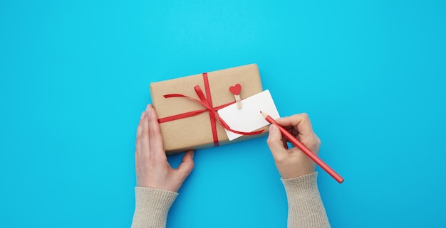 Female hand holds a box wrapped in brown kraft paper and tied with a silk red ribbon