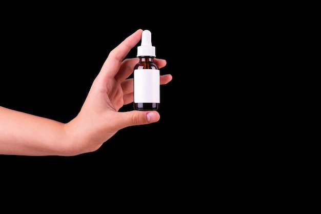 Female hand holds brown glass bottle with a pipette on a black background top view Organic natural