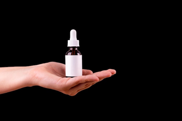 Female hand holds brown glass bottle with a pipette on a black background top view Organic natural