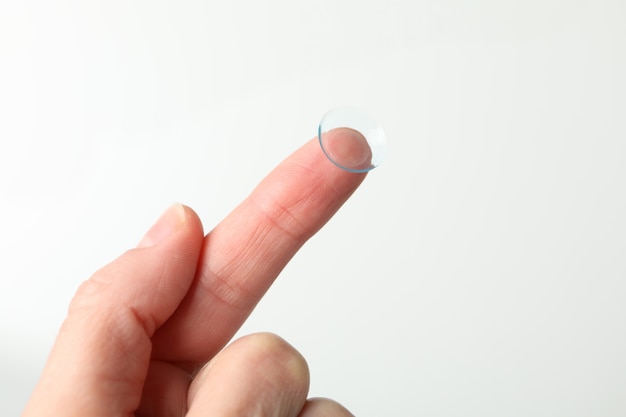 Female hand holds contact lens on white surface, close up