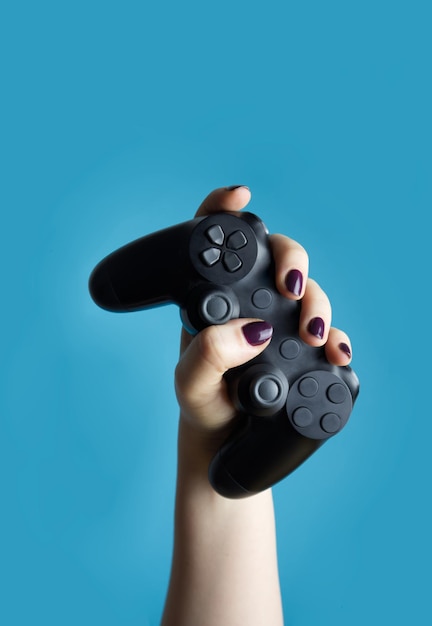 Foto una mano femminile tiene un controller da una console video su uno sfondo blu in primo piano