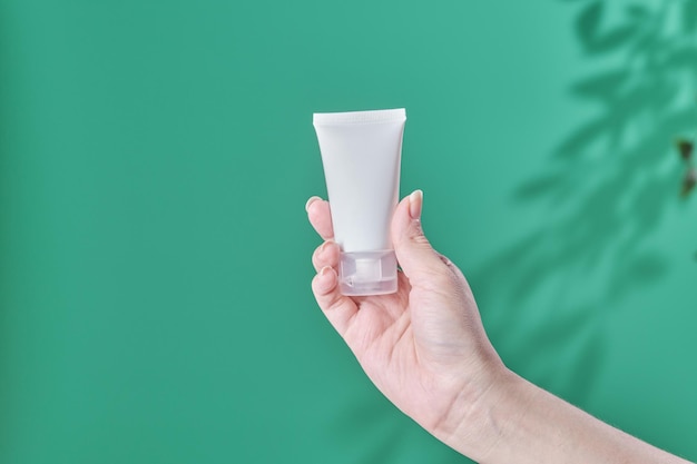 La mano femminile tiene il prodotto cosmetico in tubo di vetro lozione idratante antietà olio essenziale per il viso o siero su sfondo verde con ombra leggera natura bellezza cosmetico concetto di cura della pelle