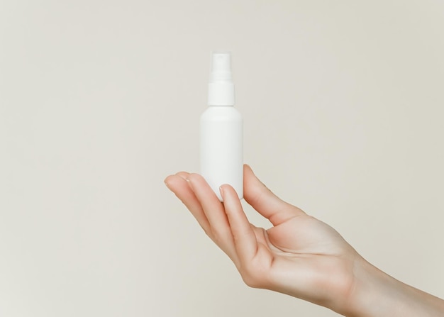 Photo a female hand holds and demonstrates a white spray bottle on a gray background