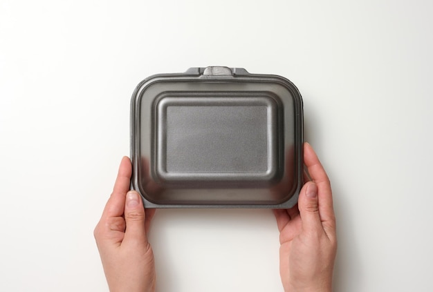 Female hand holds a disposable food container. Gray box of polystyrene on a white background