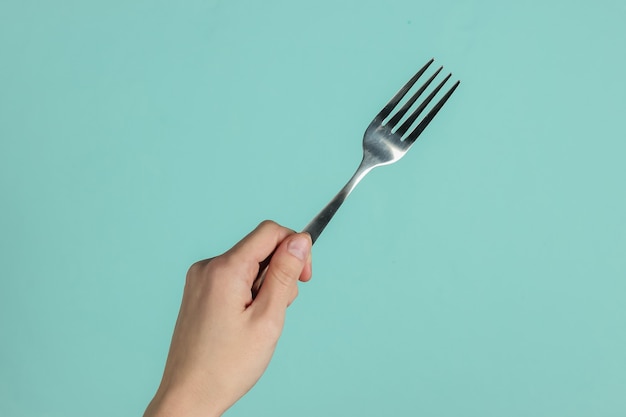 Mano femminile tiene una forchetta su sfondo blu pastello. vista dall'alto. studio girato