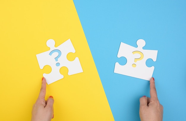 Female hand holds a fragment of a white large puzzle on a yellow blue background