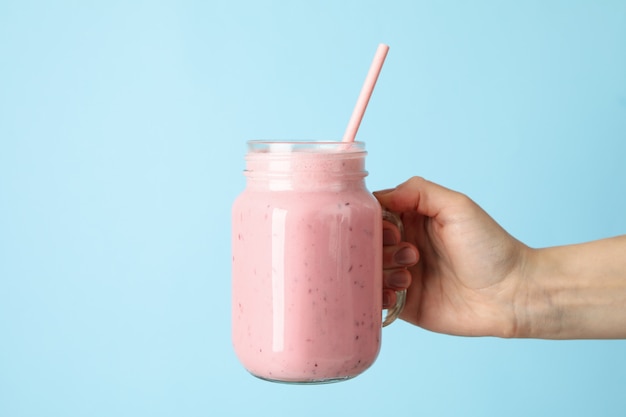 Female hand holds glass jar of strawberry milkshake on blue background