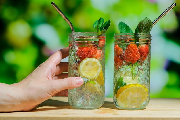 Female hand holds glass of refreshing summer infused water with fresh fruits