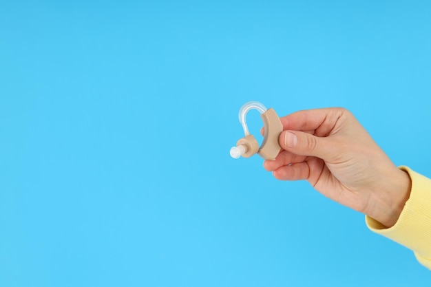 La mano femminile tiene l'apparecchio acustico su sfondo blu